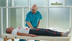 A person in blue medical scrubs performing biomagnetism therapy on a patient lying on a treatment table with magnets placed on various parts of the body.