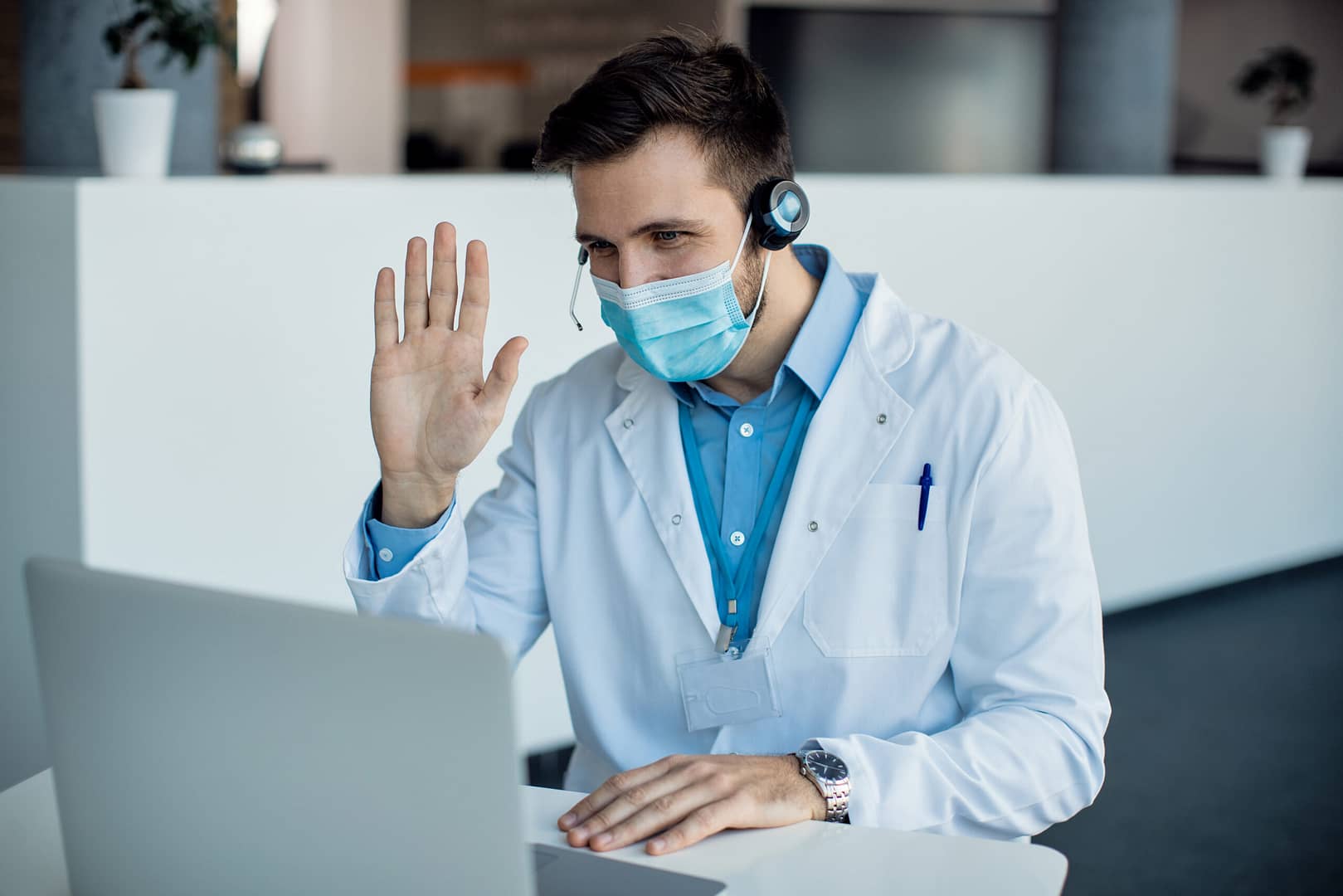 Male doctor waving during a video call over laptop  at medical c