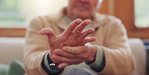 An elderly person holding their hand in pain, highlighting biomagnetism therapy for arthritis relief